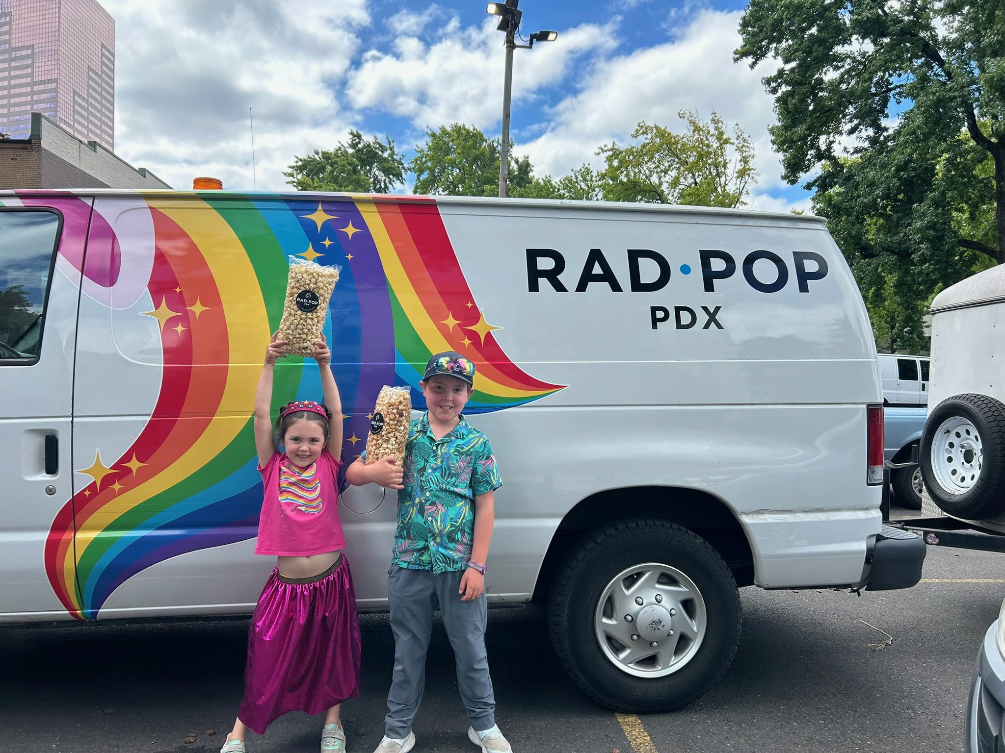 Two kids holding Rad Pop popcorn in front of the Rad Pop rainbow van