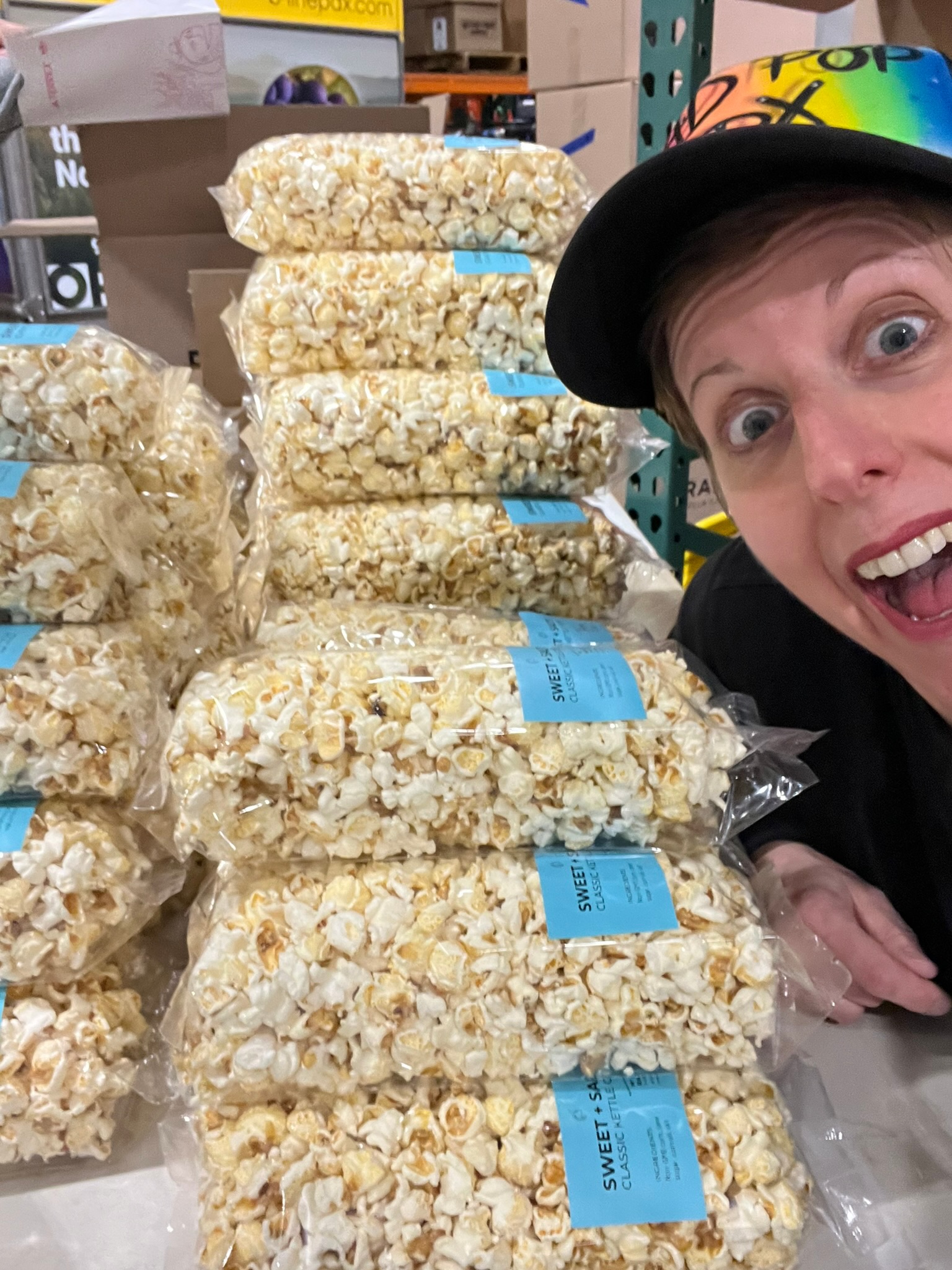 Katie smiling beside stacks of full-size Sweet + Salty popcorn bags